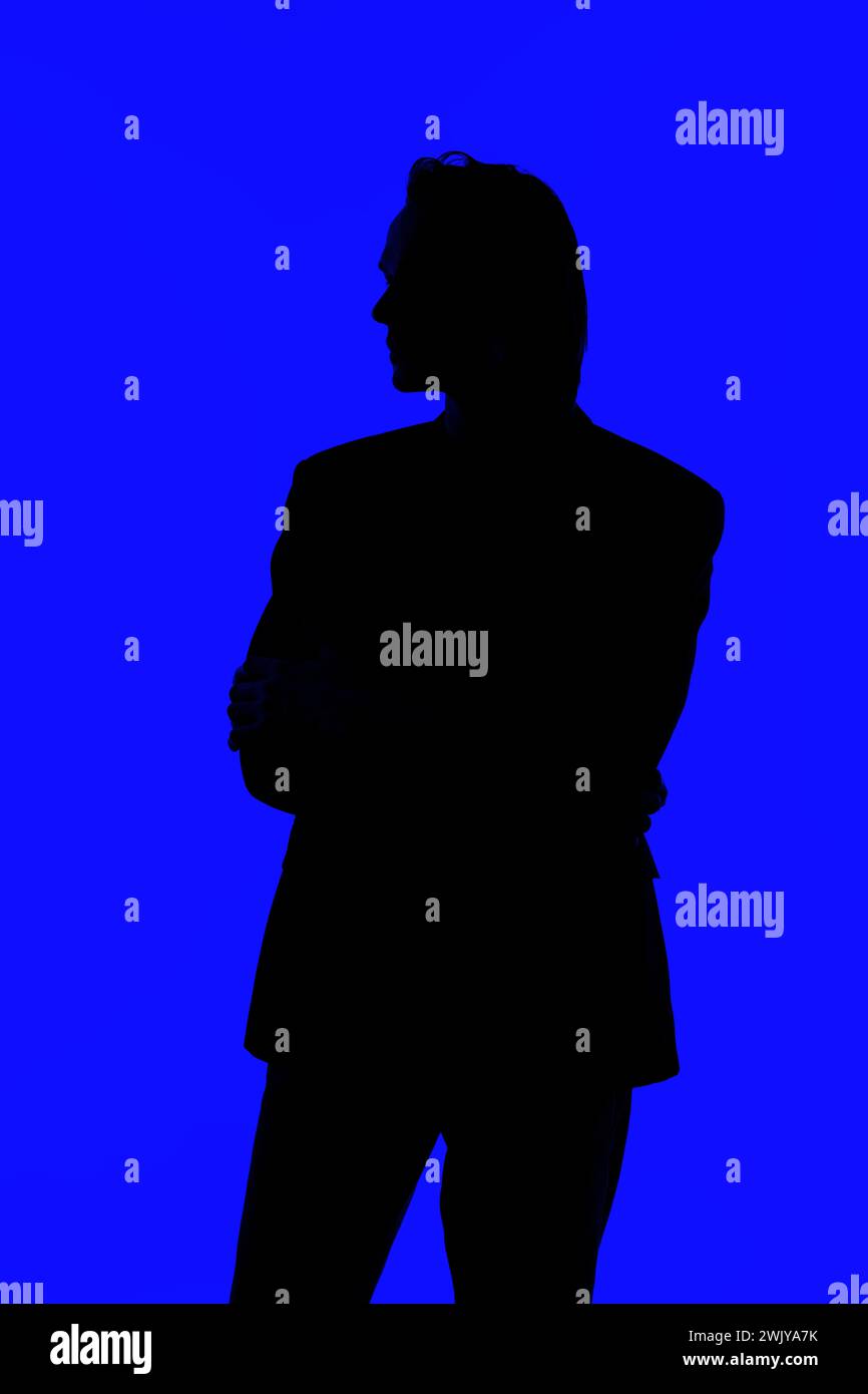 Misteriosa silhouette di un bell'uomo con occhiali da vista in una giacca su uno sfondo blu brillante Foto Stock