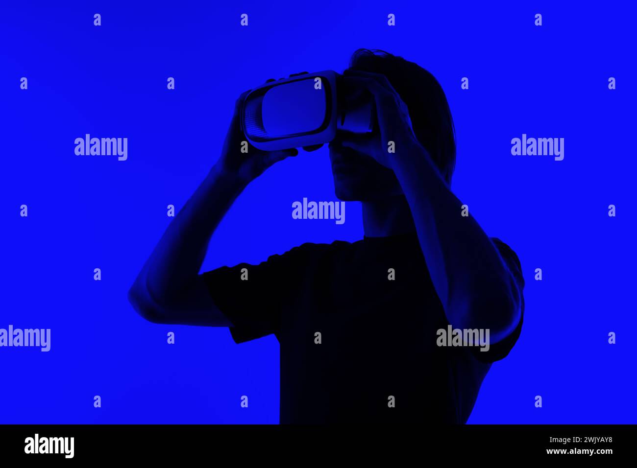 Silhouette in un giovane irriconoscibile che indossa occhiali di protezione per la realtà virtuale su uno sfondo blu luminoso, un concetto futuristico di metaversa Foto Stock