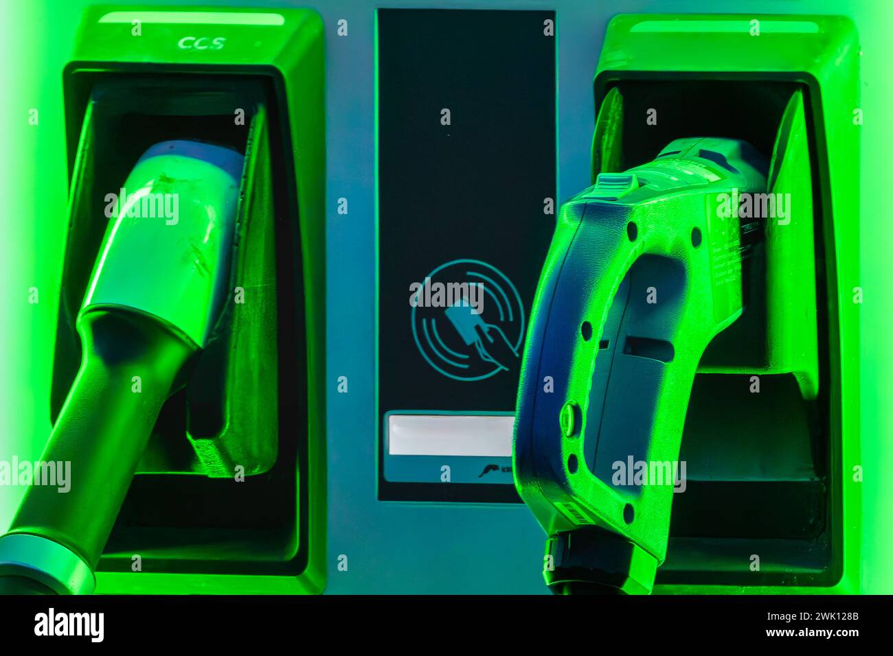 Un'auto elettrica che si ricarica in una stazione con un caricabatterie elettrico e una luce verde Foto Stock