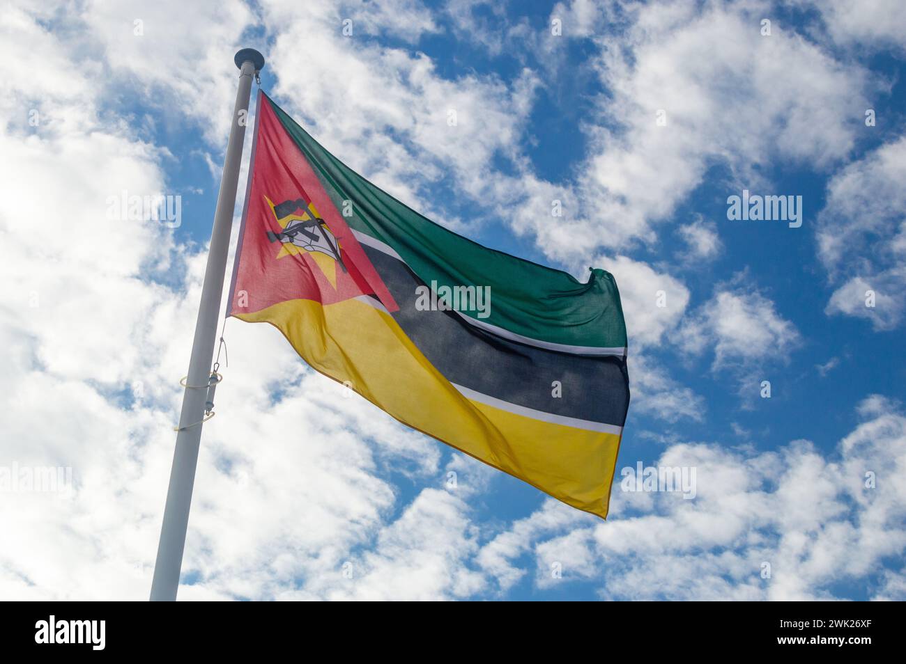 Bandiera del Mozambico che sventola nel vento. Bandiera nazionale della Repubblica del Mozambico. Bandiera con fucile Kalashnikov e zappa, sovrapposta a un libro aperto. Foto Stock