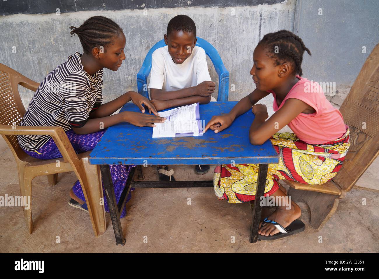 Gruppo di bambini africani della scuola elemantica che preparano la lezione condividendo un libro; concetto di libro di testo e forniture scolastiche scarsità nello sviluppo di co Foto Stock