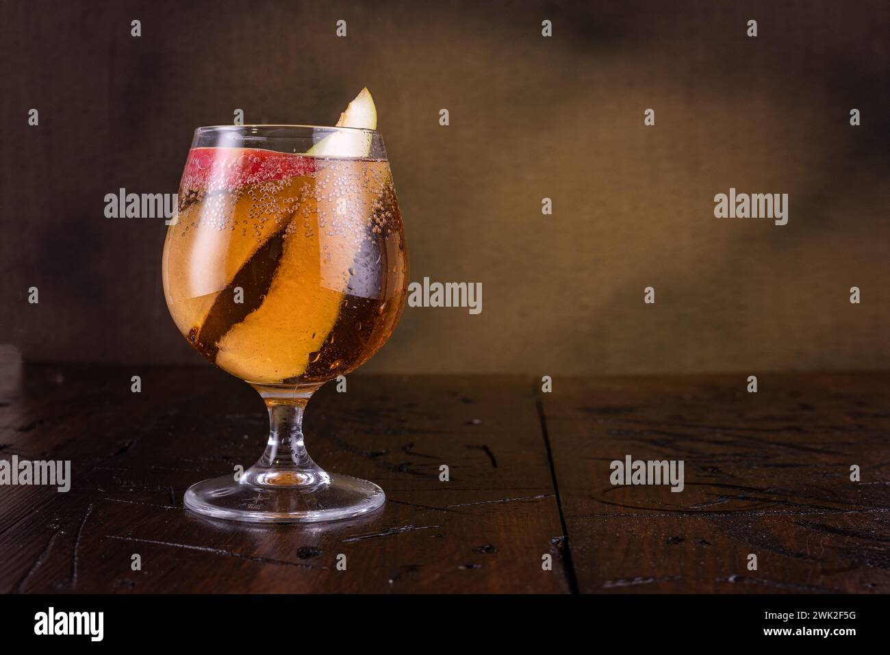 Bicchiere con una bevanda su sfondo marrone. Bicchiere con fette di frutta. Bevete sul tavolo. Copia spazio. Foto Stock