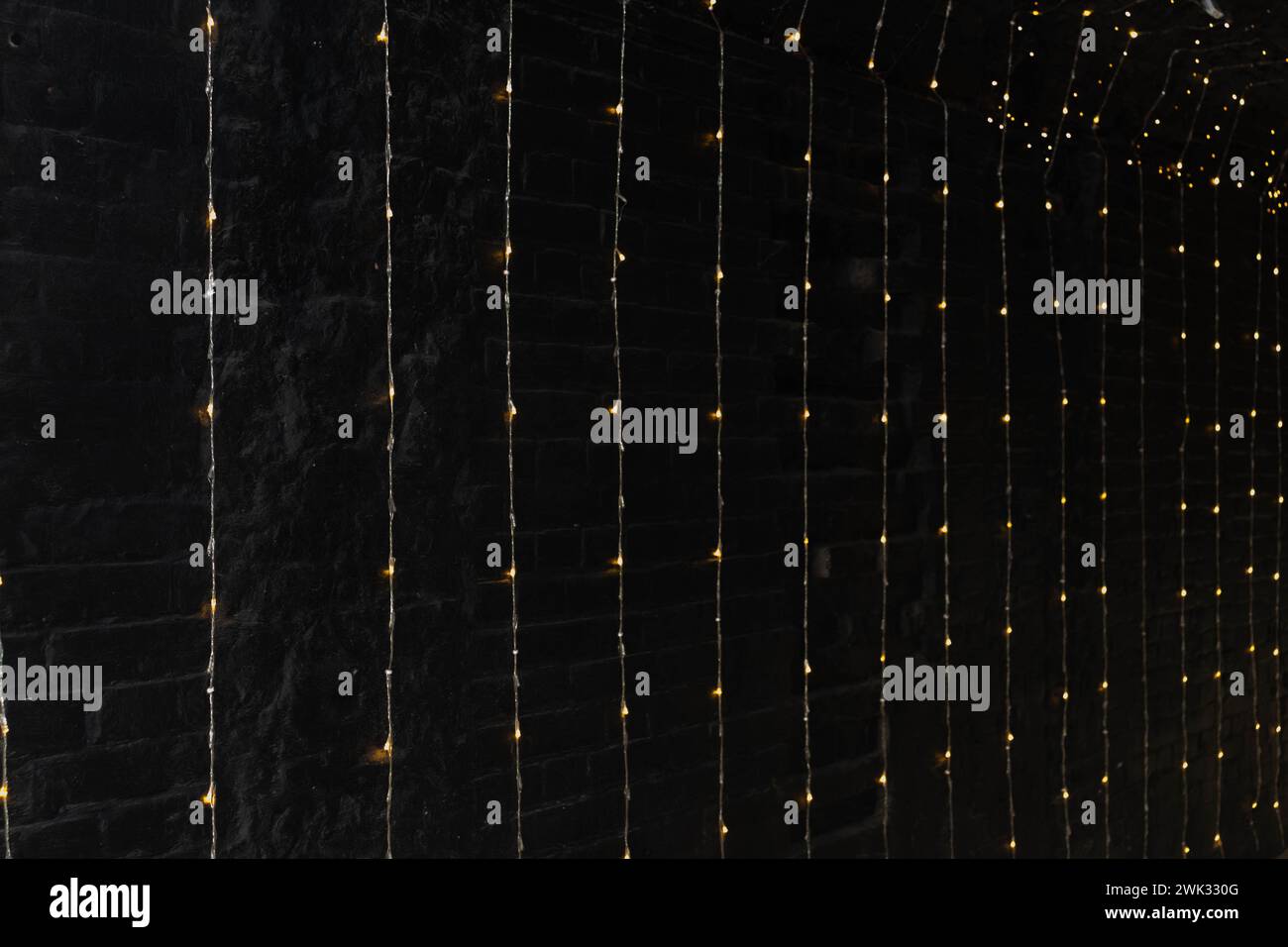 Illuminazione a LED di muratura in muratura, ghirlanda elettrica su sfondo in mattoni neri Foto Stock