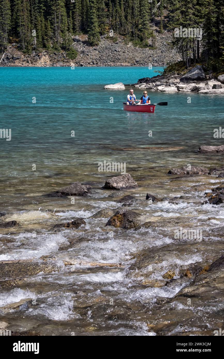 Coppia in canoa di fronte al fiume turbolento che entra nel lago glaciale Moraine nel Banff National Park, Alberta, Canada il 5 giugno 2023 Foto Stock