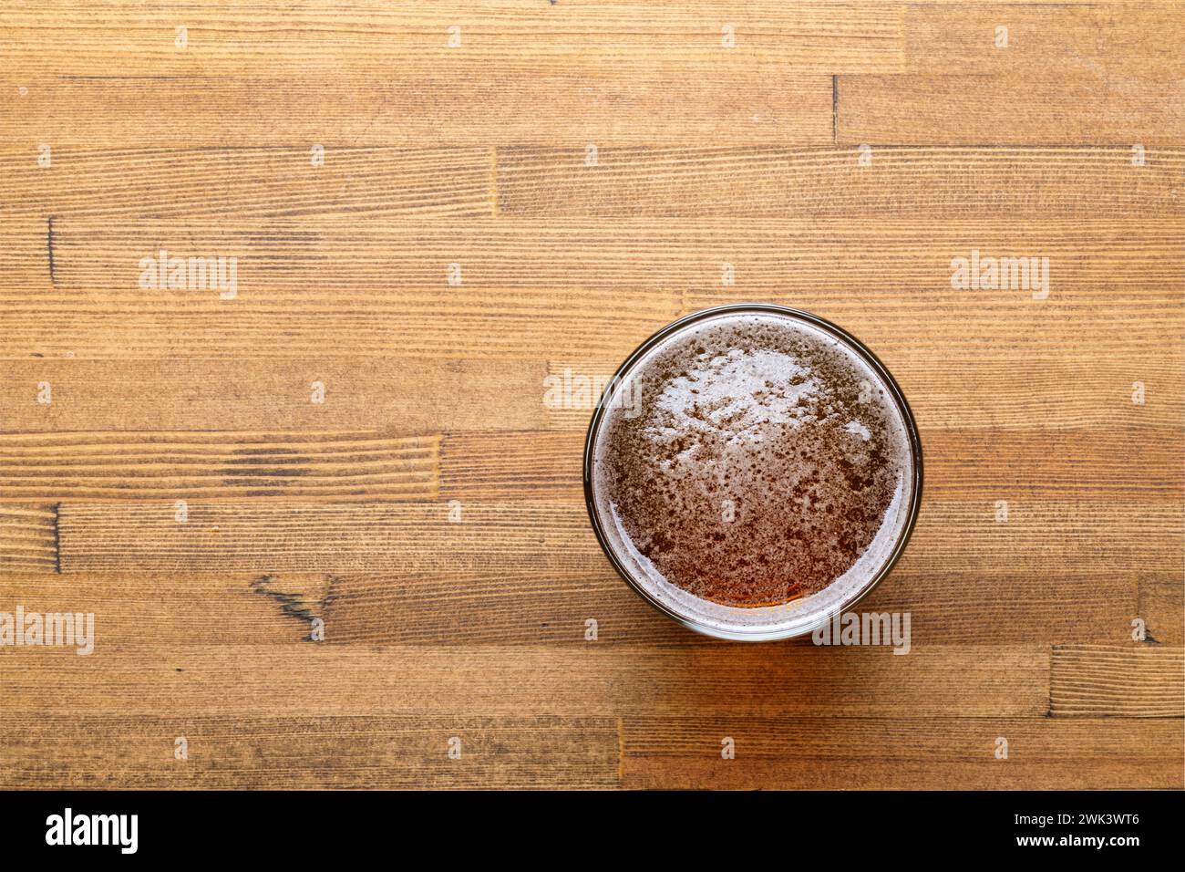 Vista dall'alto verso il basso di una birra artigianale appena versata in un bicchiere posto su un tavolo in legno dai toni caldi Foto Stock