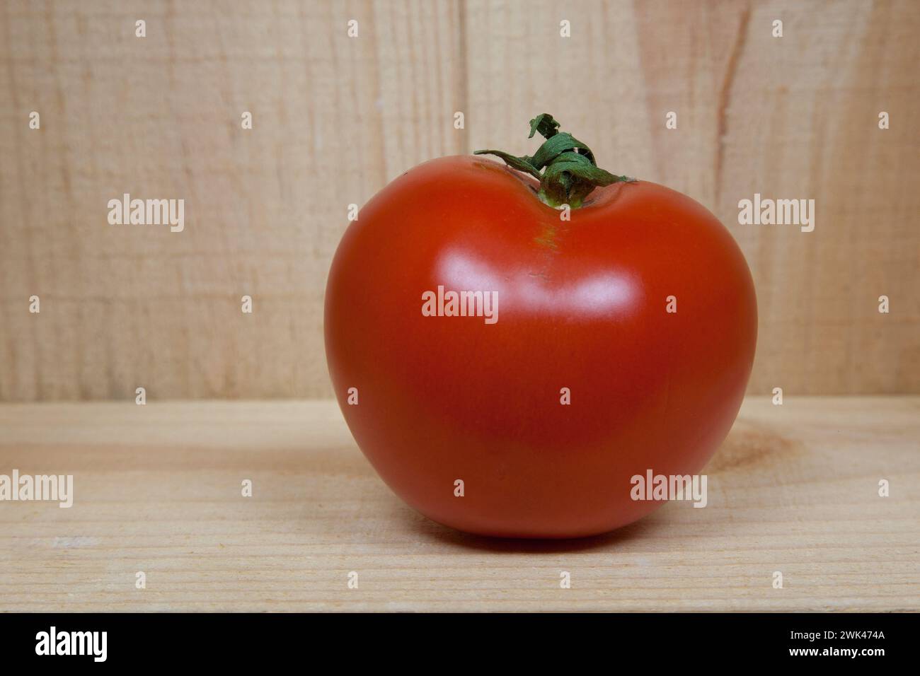 Nella foto, un pomodoro giace in una scatola di legno rustica, i cui colori caldi sottolineano la freschezza del frutto rosso. Foto Stock