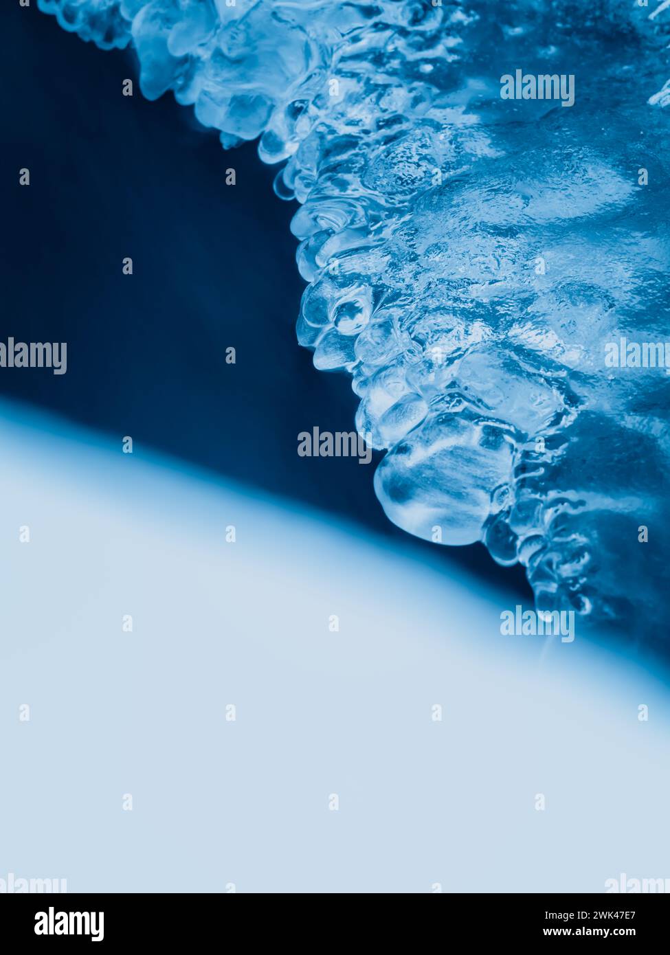 Questa immagine cattura gli intricati dettagli dei ghiacciai aggrappati a un bordo congelato, su uno sfondo blu morbido e sfocato che accentua il ghiaccio Foto Stock
