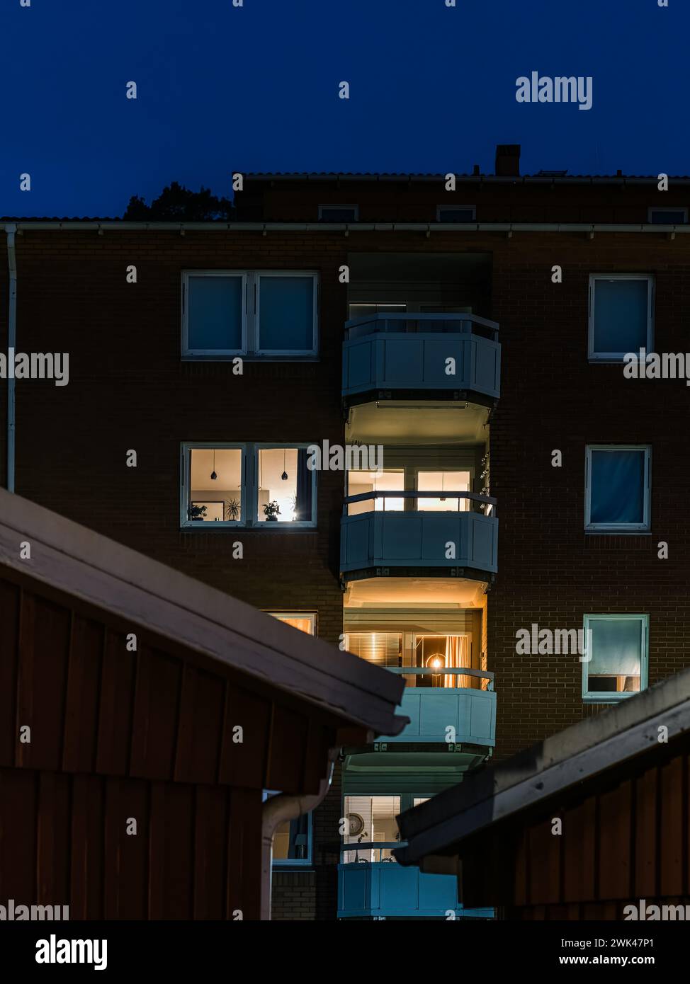 Questa immagine cattura l'esterno di un edificio residenziale al crepuscolo, con la luce calda che splende da alcune finestre e balconi degli appartamenti, hig Foto Stock