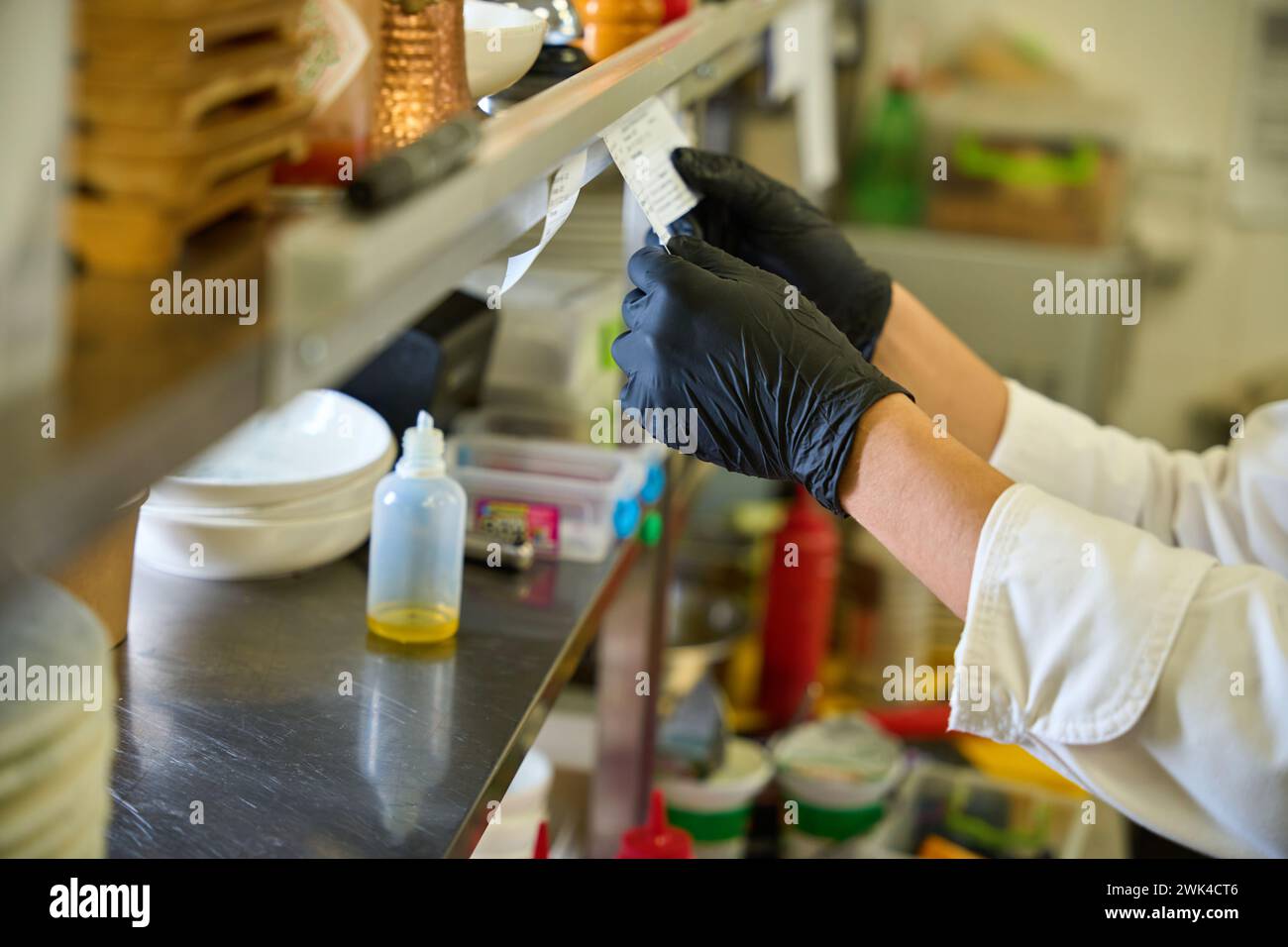 Il lavoratore della cucina con guanti protettivi neri guarda attraverso una ricevuta Foto Stock