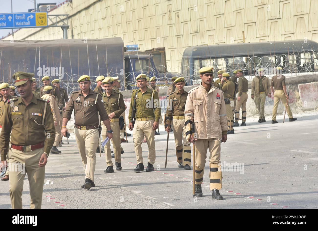 GHAZIABAD, INDIA - 18 FEBBRAIO: Il personale di polizia è in guardia accanto a una barriera per impedire agli agricoltori di protestare per chiedere prezzi minimi del raccolto di marciare verso la capitale nazionale al confine di Ghazipur, il 18 febbraio 2024 a Ghaziabad, India. Sono stati effettuati massicci dispiegamenti di polizia e personale paramilitare, oltre alla barricata multilivello, per sigillare i confini della capitale nazionale a Singhu, Tikri e Ghazipur, per impedire agli agricoltori che protestano di entrare in città durante la loro marcia prevista per il "Delhi Chalo". La polizia di Delhi ha anche imposto la sezione 144 della procedura penale Co Foto Stock