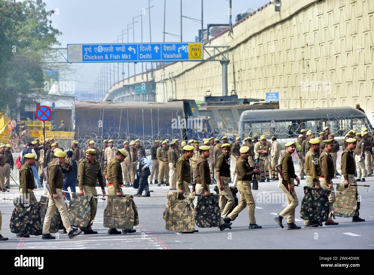 GHAZIABAD, INDIA - 18 FEBBRAIO: Il personale di polizia è in guardia accanto a una barriera per impedire agli agricoltori di protestare per chiedere prezzi minimi del raccolto di marciare verso la capitale nazionale al confine di Ghazipur, il 18 febbraio 2024 a Ghaziabad, India. Sono stati effettuati massicci dispiegamenti di polizia e personale paramilitare, oltre alla barricata multilivello, per sigillare i confini della capitale nazionale a Singhu, Tikri e Ghazipur, per impedire agli agricoltori che protestano di entrare in città durante la loro marcia prevista per il "Delhi Chalo". La polizia di Delhi ha anche imposto la sezione 144 della procedura penale Co Foto Stock