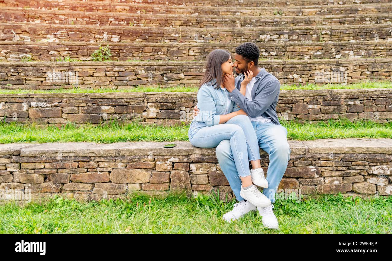 Un bell'uomo che sussurra a una bella donna sorridente quanto la ami mentre sono seduti nel parco Foto Stock