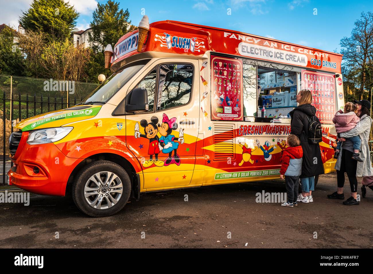 Persone che acquistano gelati da un pulmino elettrico per gelati in un soleggiato pomeriggio invernale. Eco-compatibile, camion elettrico, fornitore, Galles, Cardiff. Foto Stock