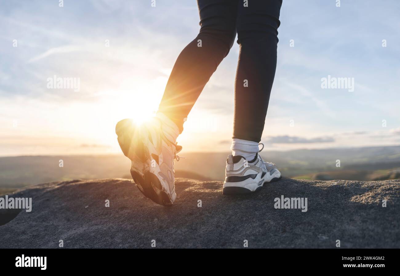 Primo piano di un escursionista in allenatori, trekking in montagna al tramonto. Concetto di esercizio, fitness e stile di vita sano e attivo immagine tonificata Foto Stock