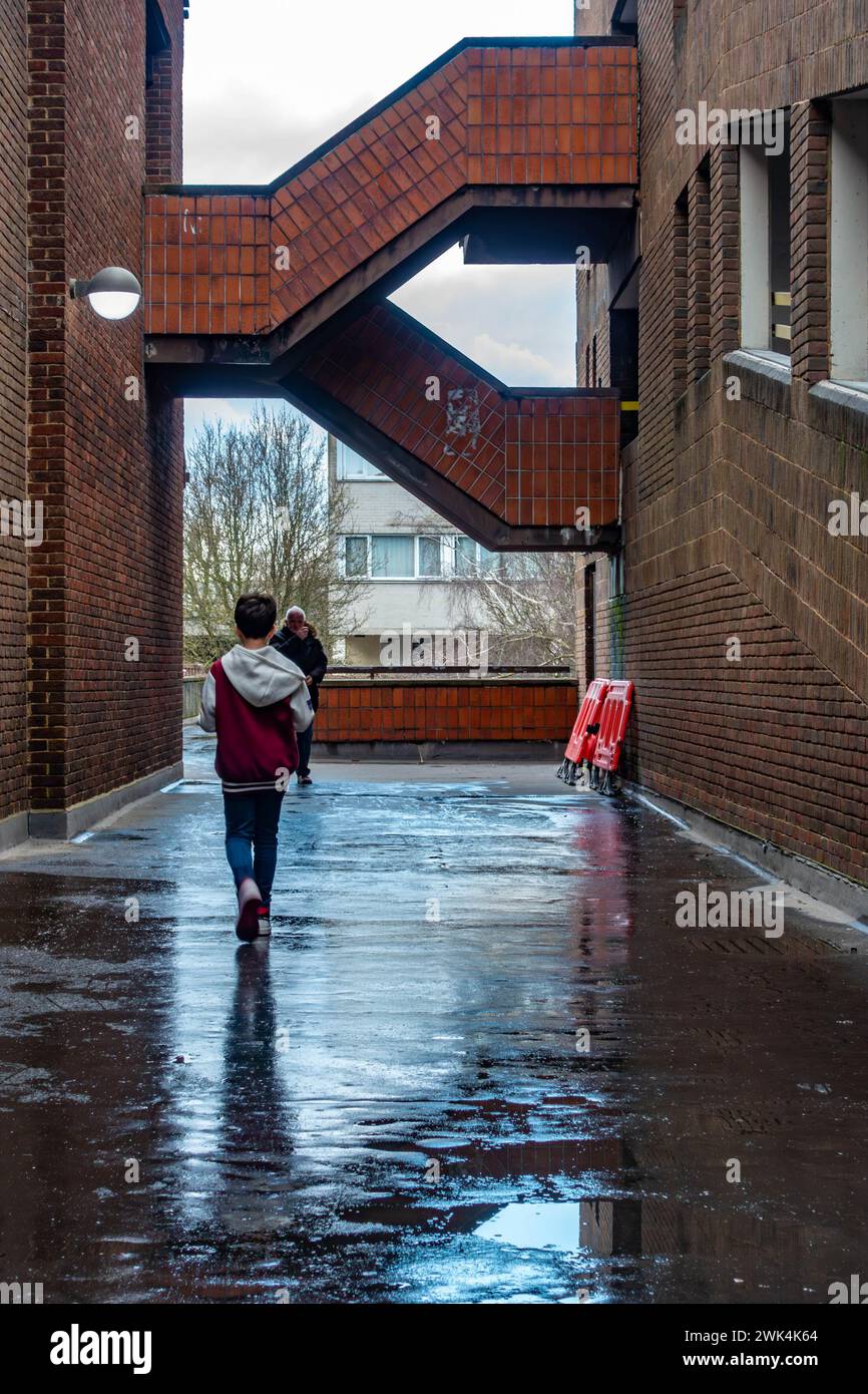 Un ragazzo che cammina lungo un sentiero che passa sotto un ponte con un forte design angolare, dirigendosi fuori da Windsor Yards verso Ward Royal a Windsor, Regno Unito Foto Stock