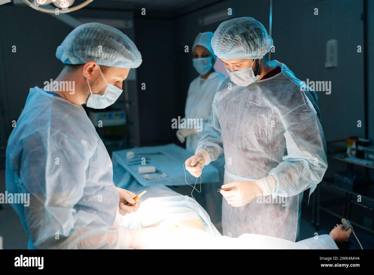 Team multietnico di chirurghi professionisti e infermieri in uniforme sul posto di lavoro in sala operatoria, che esegue interventi di trapianto di cuore in condizioni di luminosità Foto Stock