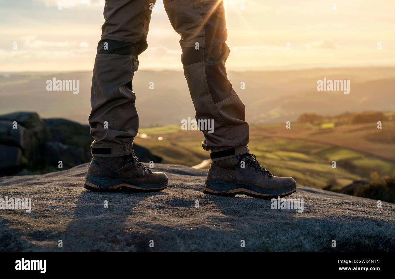 Uomo con stivali speciali che cammina tra le montagne raggiungendo la destinazione e sulla cima della montagna nel Peak District al tramonto il giorno autunnale Travel Life Foto Stock