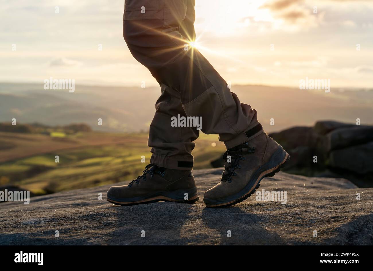 Uomo con stivali speciali che cammina tra le montagne raggiungendo la destinazione e sulla cima della montagna nel Peak District al tramonto il giorno autunnale Travel Life Foto Stock