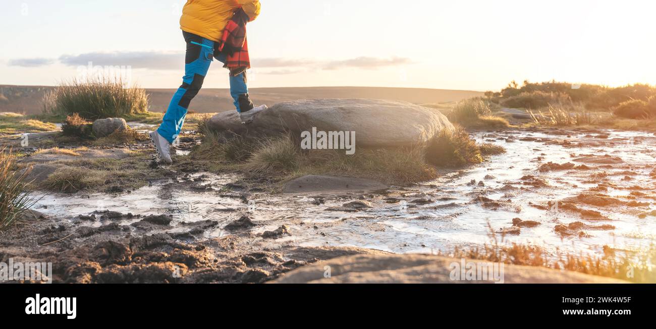 Donna energica che cammina con stivali impermeabili lungo il percorso di trekking con pozzanghere congelate nelle prime ore del mattino invernale Foto Stock