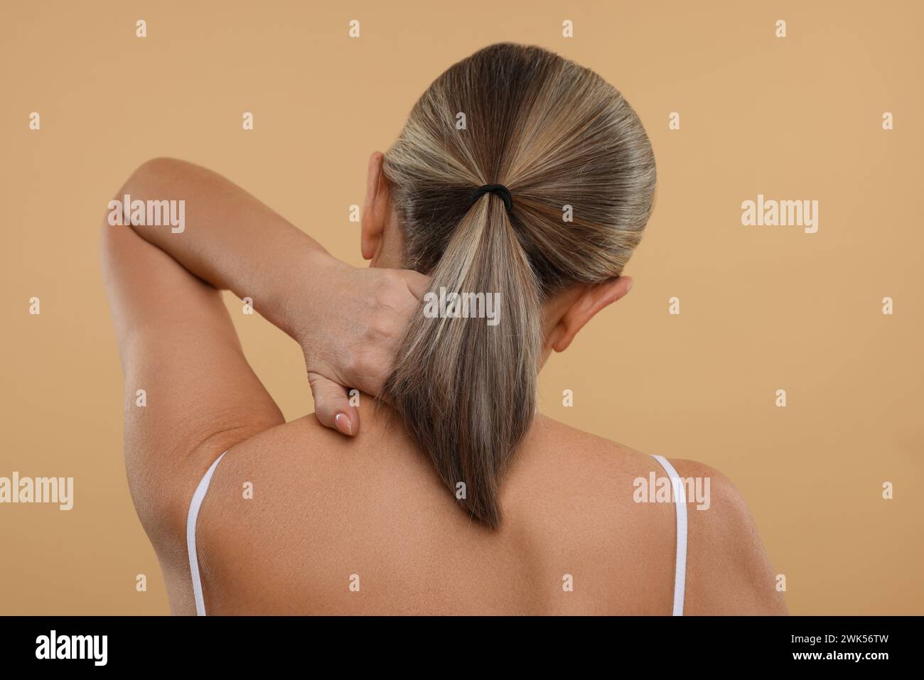 Donna matura che soffre di dolore al collo su sfondo beige, vista posteriore Foto Stock