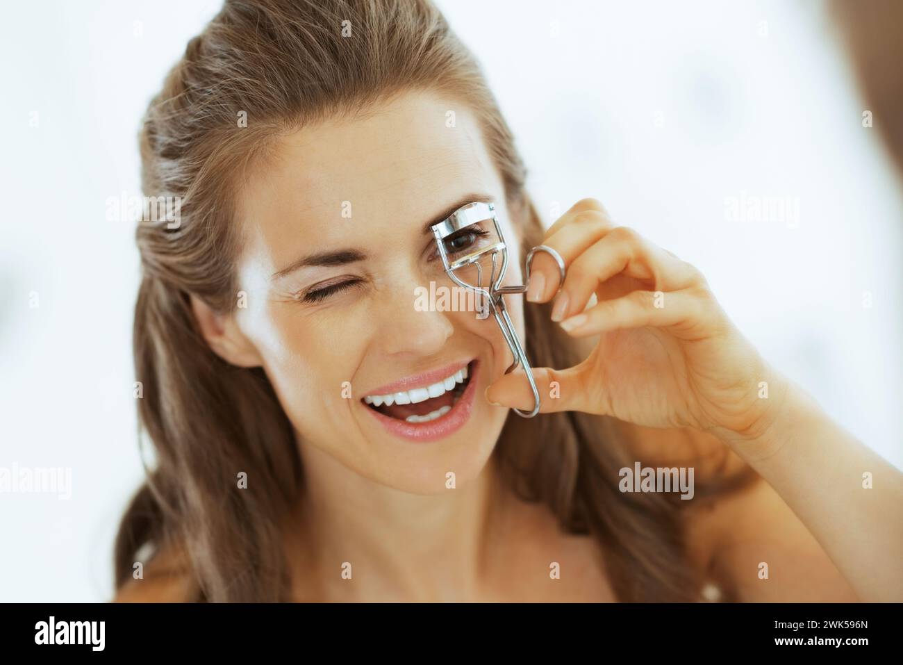 Giovane donna di ciglia utilizzando il bigodino in bagno Foto Stock