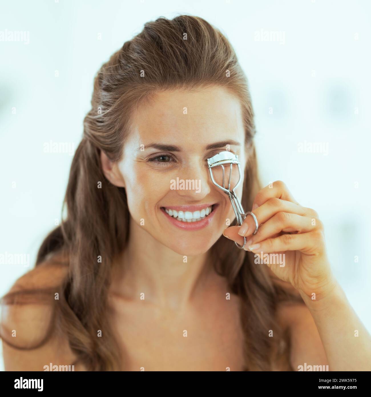 giovane donna felice che usa l'arricciacapelli ciglia in bagno Foto Stock