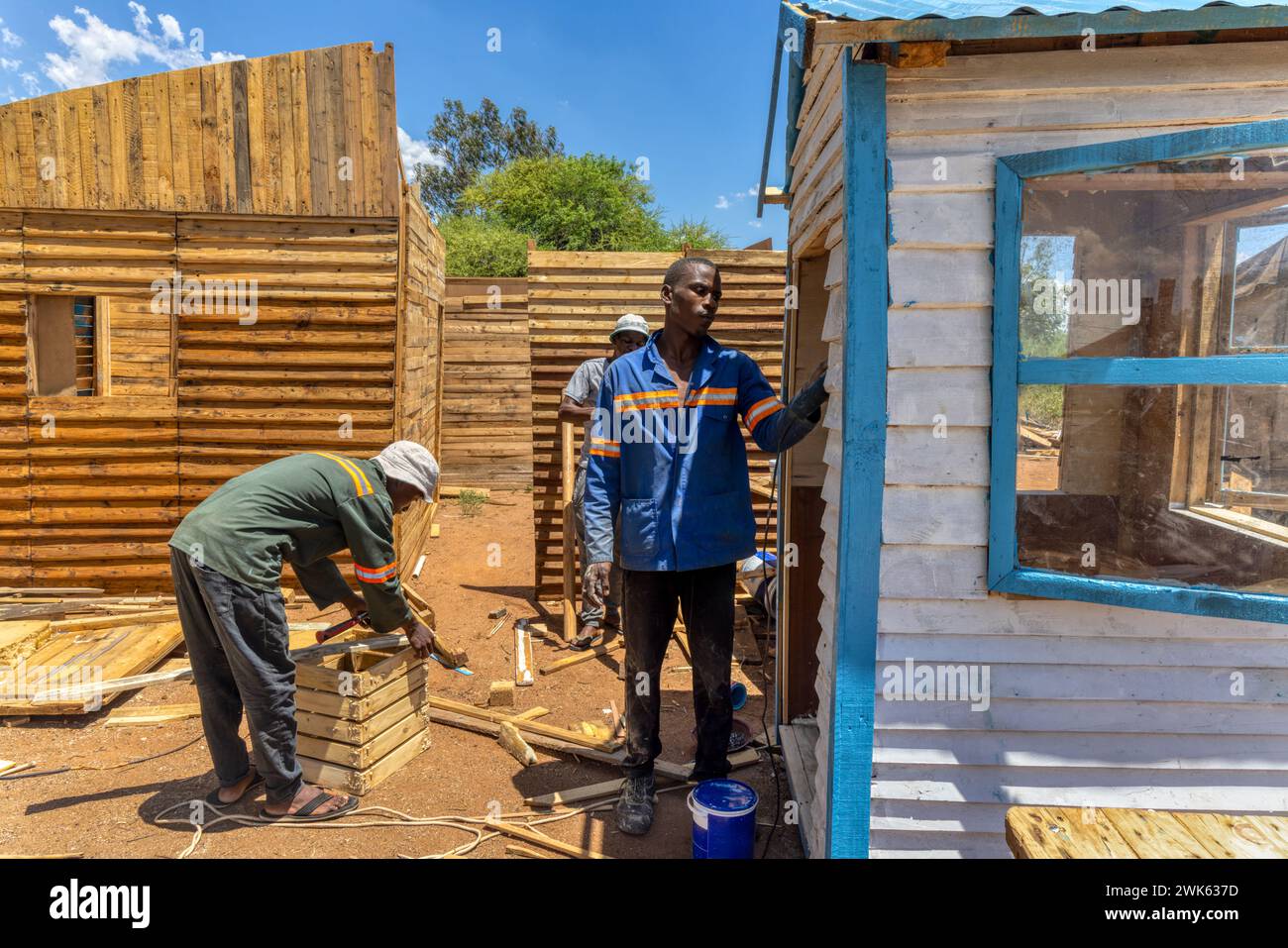 tre operai afroamericani che realizzano una casa wendy, capannoni di legno all'aperto, martellano pallet per realizzare tavole e assemblarli in pannelli Foto Stock