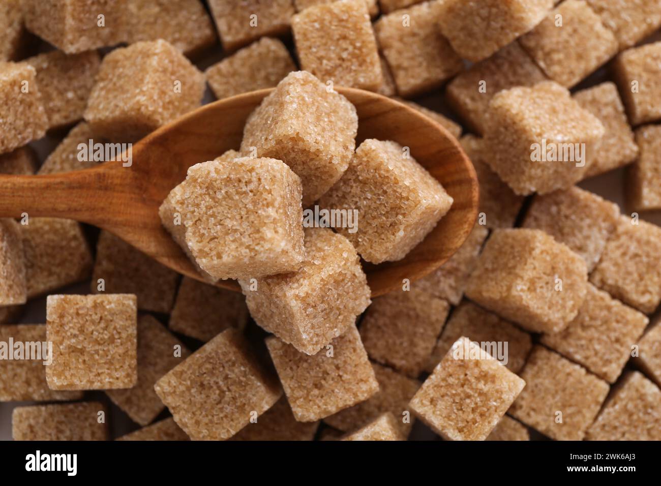 Cucchiaio di legno su cubetti di zucchero di canna, vista dall'alto Foto Stock