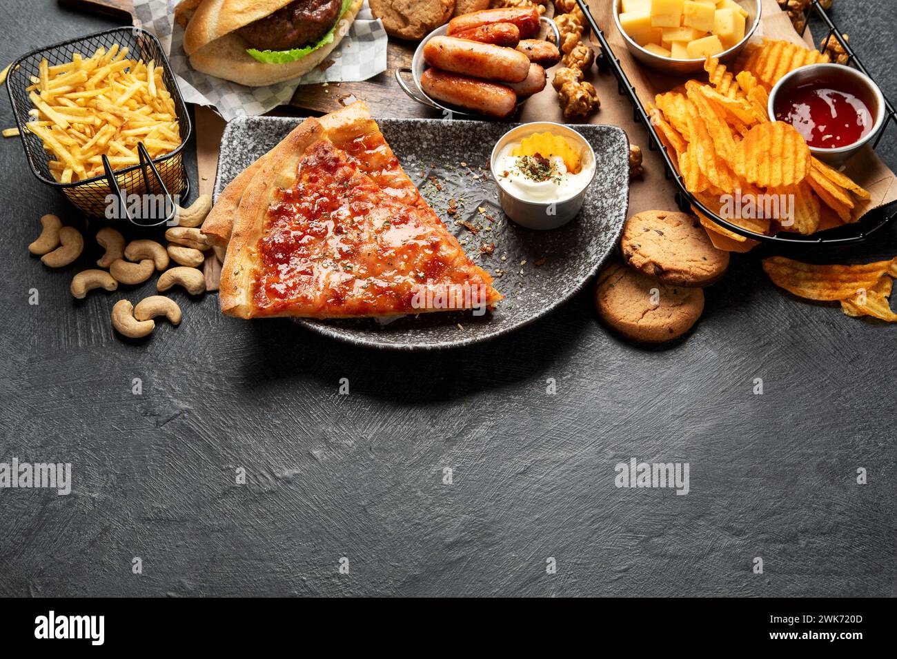 Fast food su sfondo scuro. Cibo spazzatura per il cuore e la pelle. Concetto grasso trans. Copia spazio Foto Stock