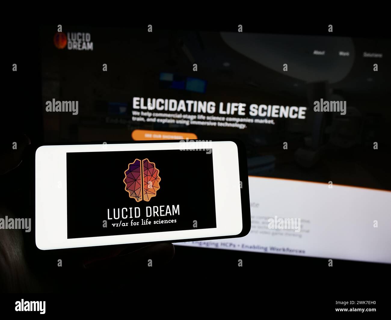 Persona che possiede uno smartphone con il logo dell'azienda statunitense di realtà virtuale VRX Studios LLC (Lucid Dream) davanti al sito Web. Mettere a fuoco il display del telefono. Foto Stock