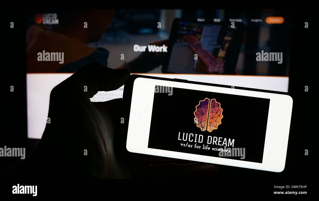 Persona che detiene un cellulare con il logo della società americana di realtà virtuale VRX Studios LLC (Lucid Dream) di fronte alla pagina web. Mettere a fuoco il display del telefono. Foto Stock