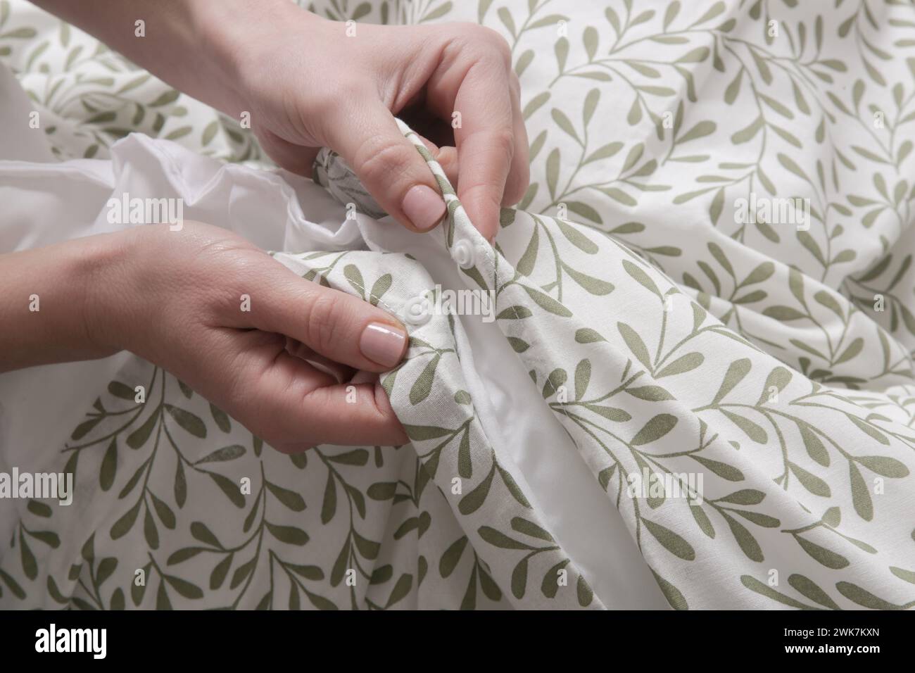 La donna sta chiudendo i bottoni sul copripiumino mentre fa il letto, da vicino Foto Stock