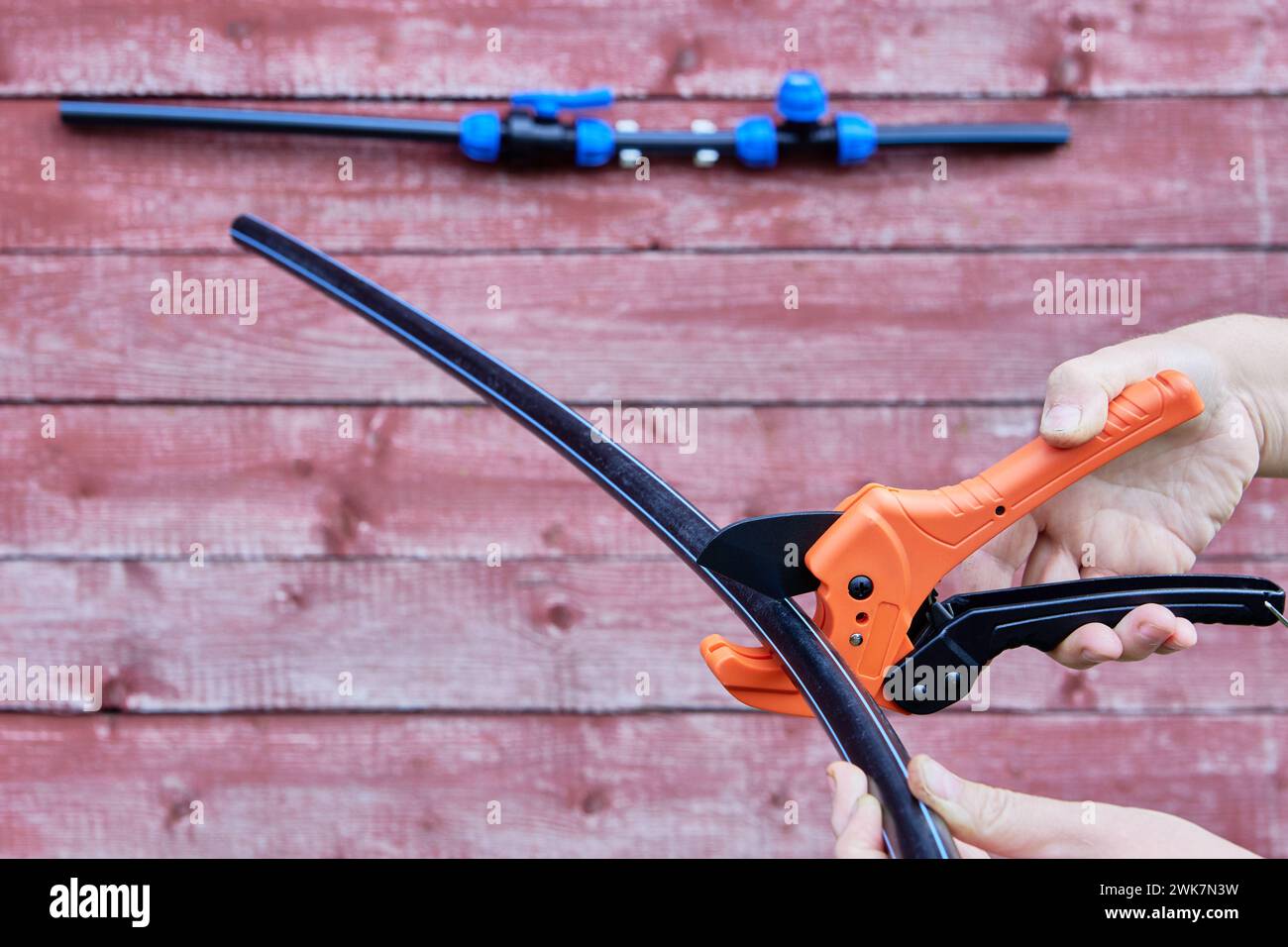 Primo piano del tagliatubi con meccanismo a cricchetto per tagliare tubi flessibili in HDPE sullo sfondo della parete rossa. Foto Stock