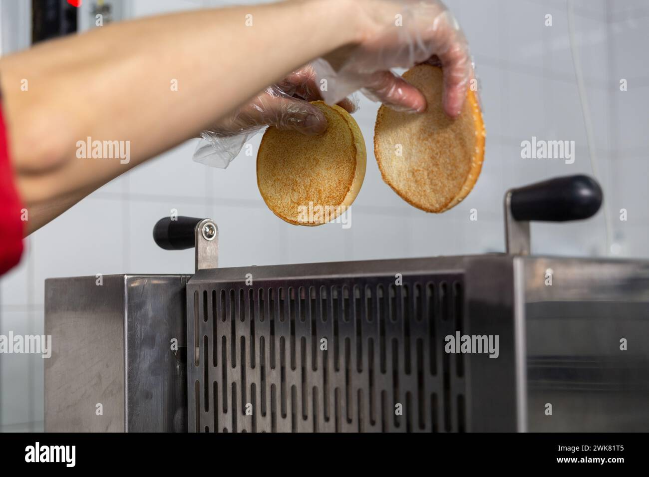 Tostapane per friggere i panini per un hamburger croccante. Il cuoco inserisce le metà del panino nel dispositivo. Foto Stock