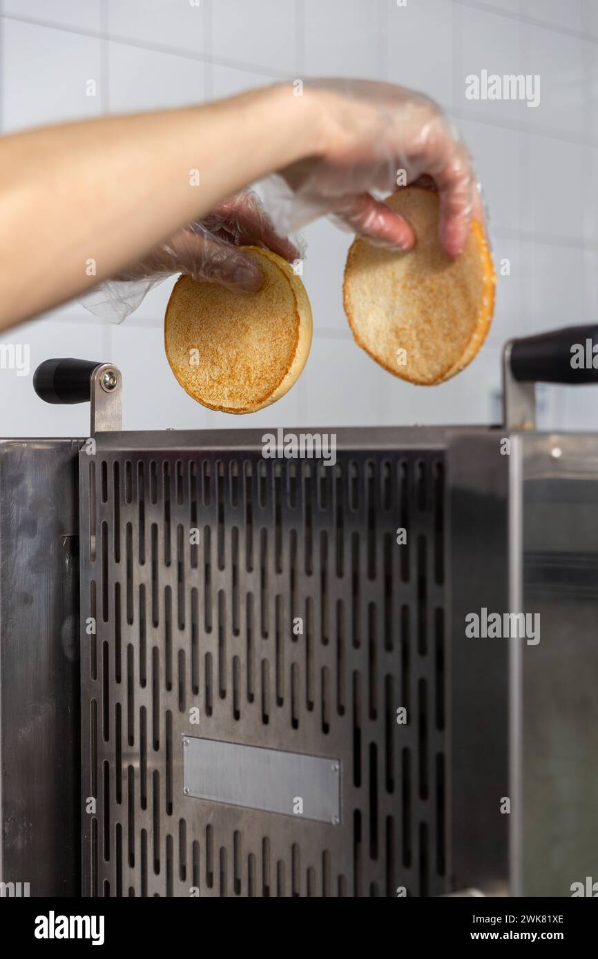 Tostapane per friggere i panini per un hamburger croccante. Il cuoco inserisce le metà del panino nel dispositivo. Foto Stock