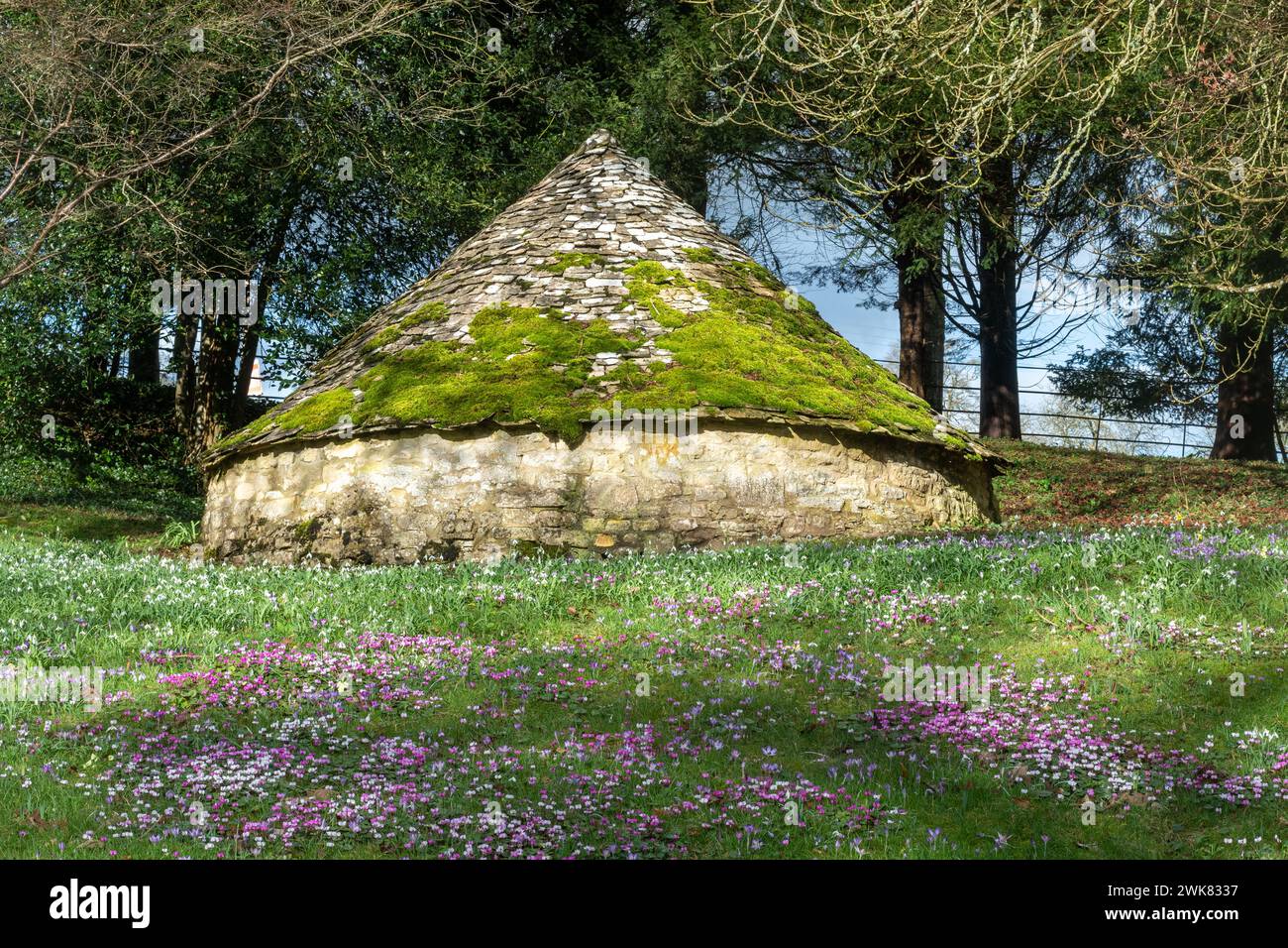 La vecchia casa di ghiaccio (icehouse) nella tenuta di campagna di Colesbourne Park con gocce di neve e fiori primaverili, Gloucestershire, Inghilterra, Regno Unito, durante febbraio Foto Stock