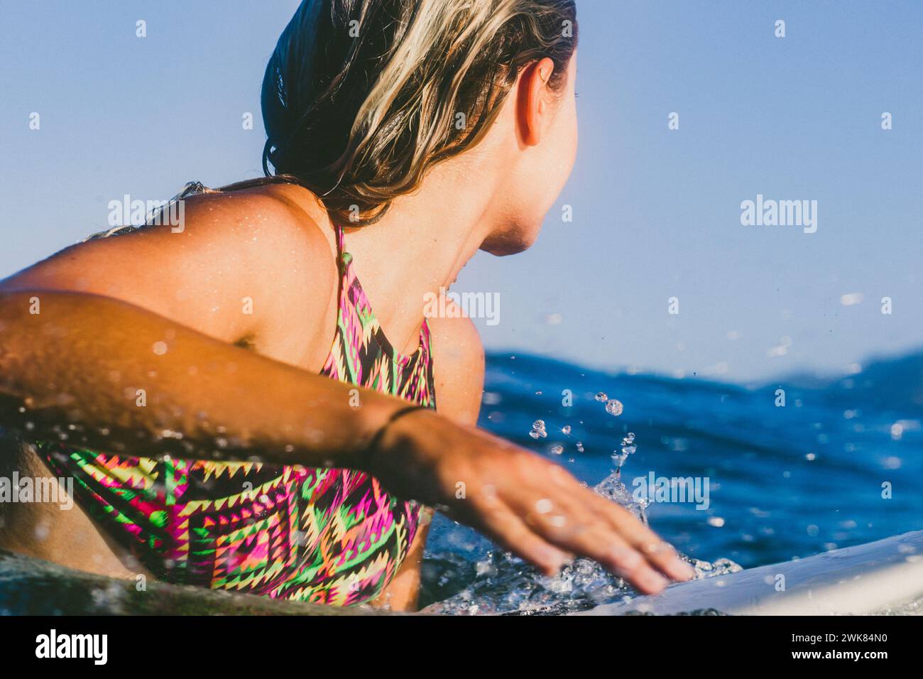 Una Surfer Paddles femminile per catturare un'onda sulla sua tavola da surf Foto Stock