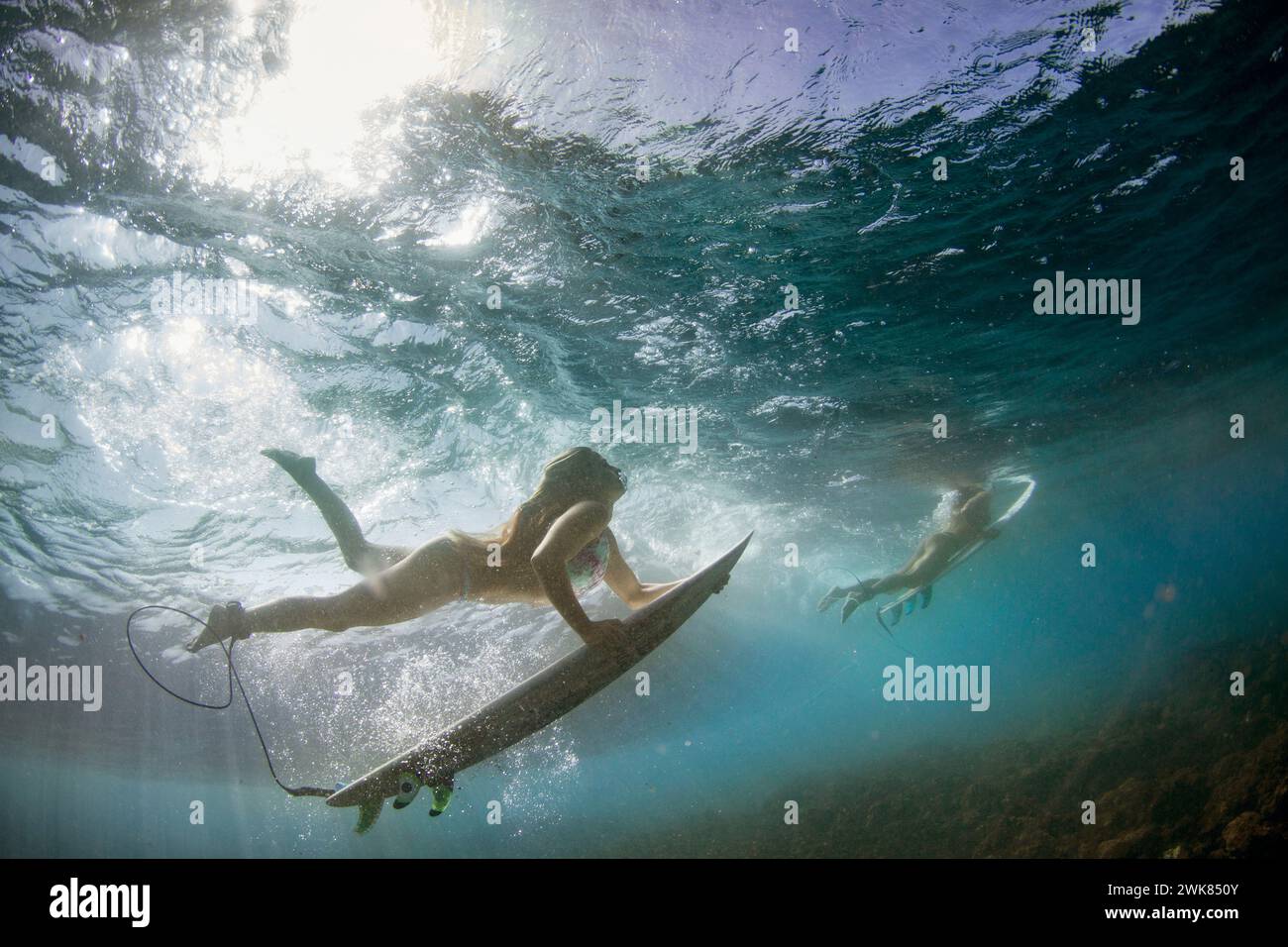 Due Surfers femminili Duck Dive sotto Un'onda Foto Stock