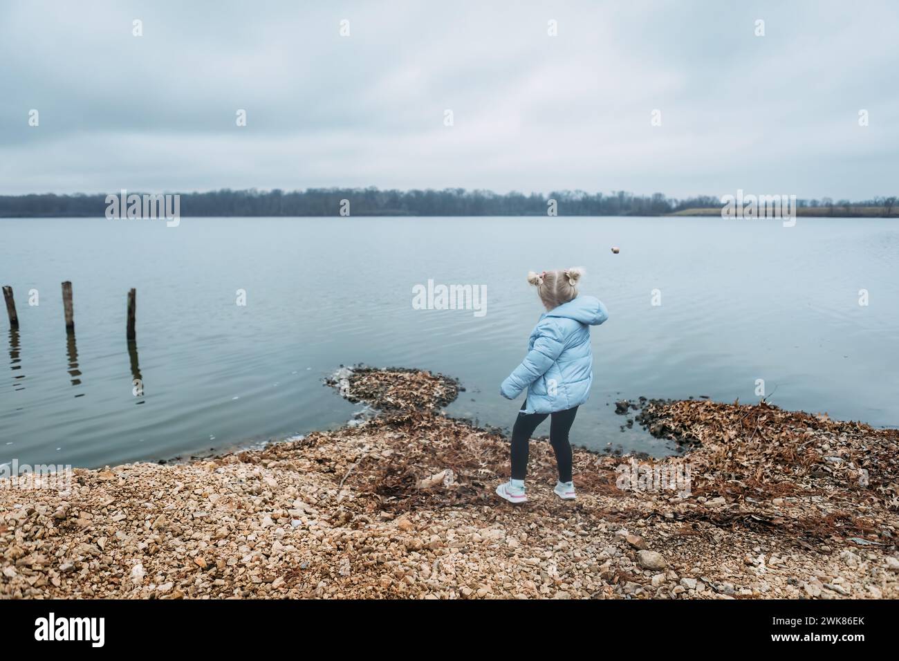 Bambino che getta rocce in acqua sulla riva del lago Foto Stock