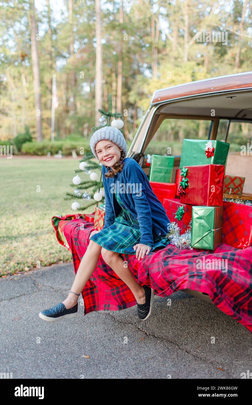 La bambina si siede sul portellone di una jeep con regali di Natale Foto Stock
