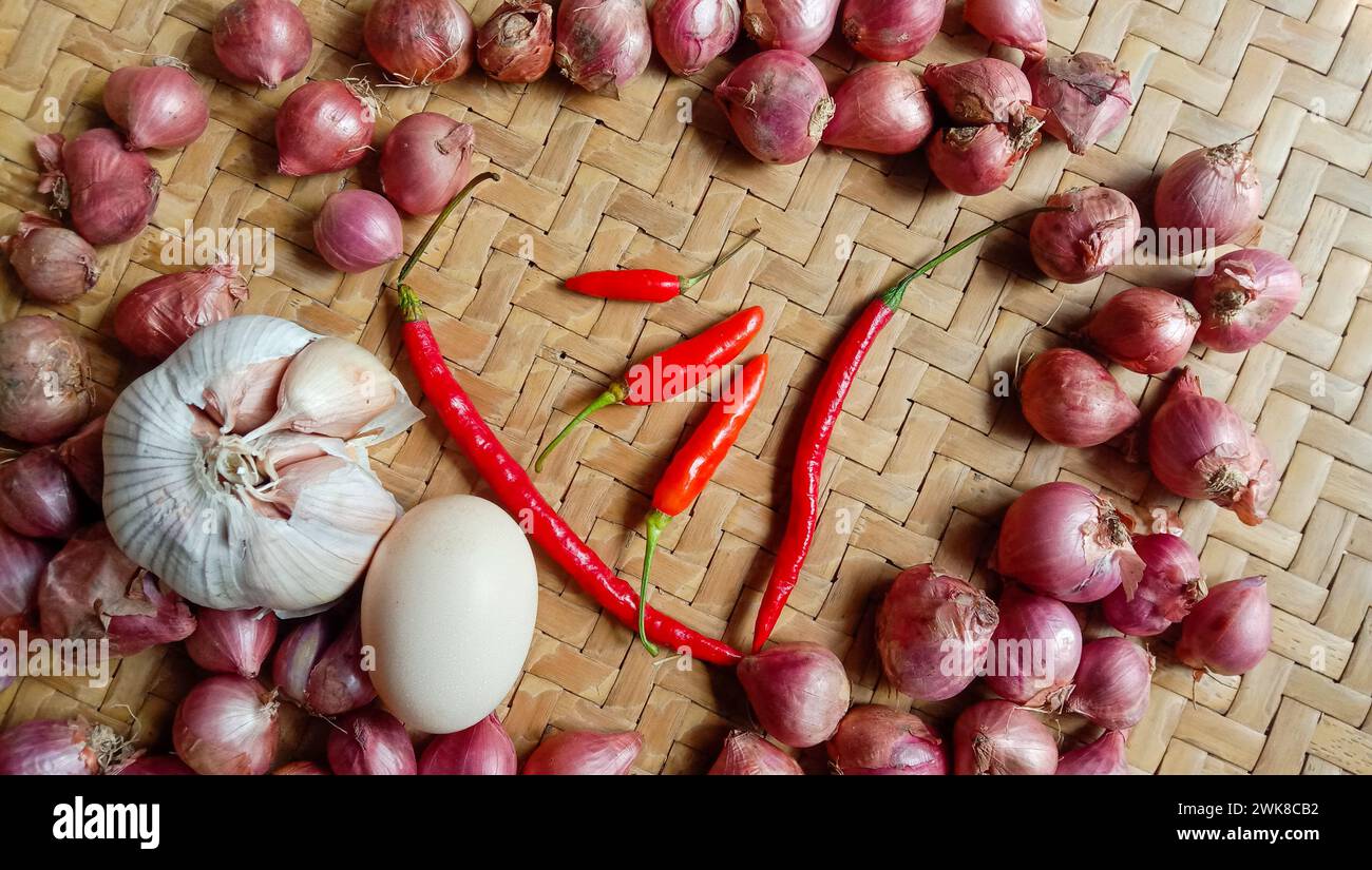 Foto di spezie sotto forma di scalogni, aglio, peperoncini e uova disposte in un bambù intrecciato Foto Stock