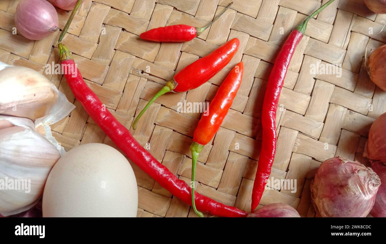 Foto di spezie sotto forma di scalogni, aglio, peperoncini e uova disposte in un bambù intrecciato Foto Stock