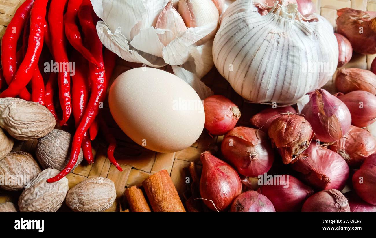Foto di spezie sotto forma di scalogni, aglio, peperoncini e uova disposte in un bambù intrecciato Foto Stock