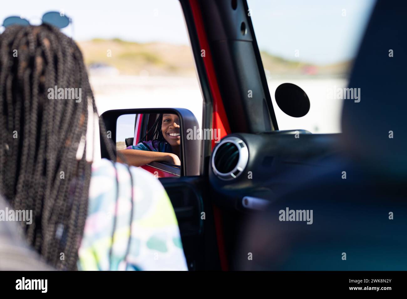 La giovane donna afroamericana sorride nello specchio laterale dell'auto durante un viaggio in auto Foto Stock