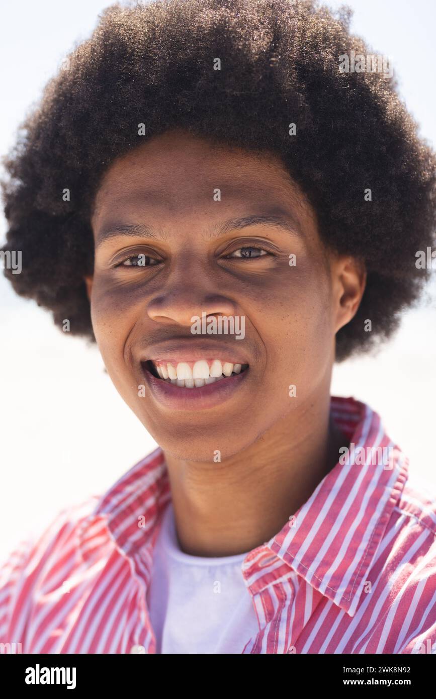 Un giovane afroamericano sorride brillantemente in spiaggia Foto Stock