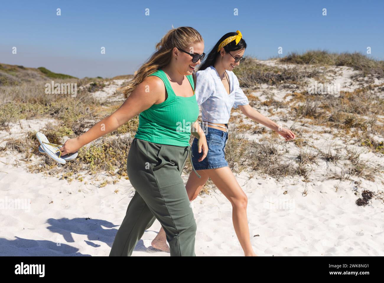 La giovane donna caucasica e la giovane donna birazziale si godono una passeggiata sulla spiaggia Foto Stock