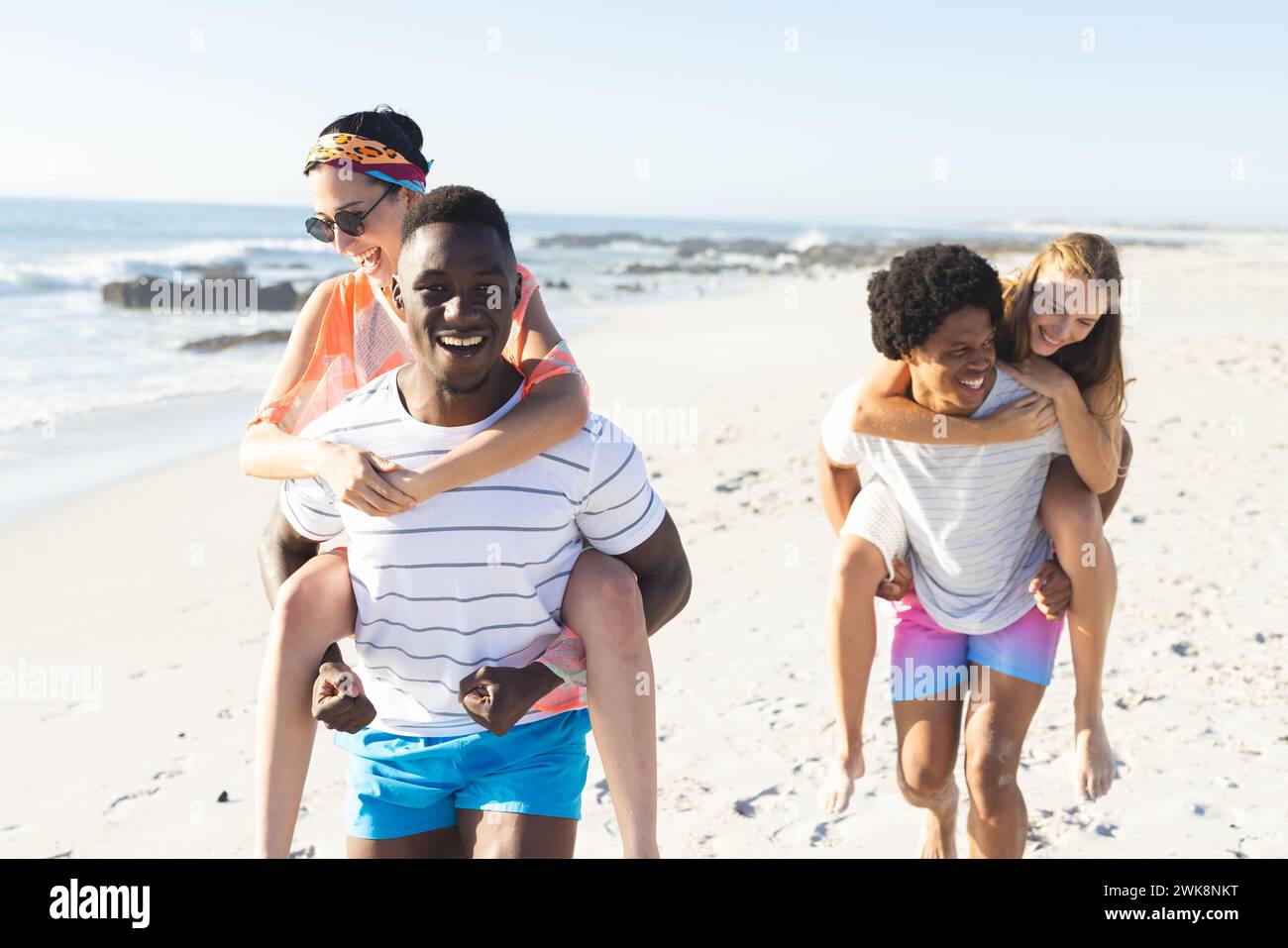 Coppie diverse possono godersi un giro in piggyback sulla spiaggia Foto Stock