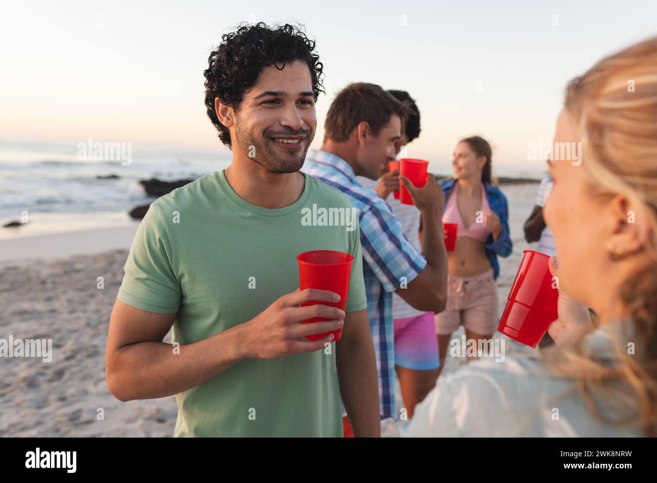 Diversi gruppi di amici si godono una festa in spiaggia al tramonto Foto Stock