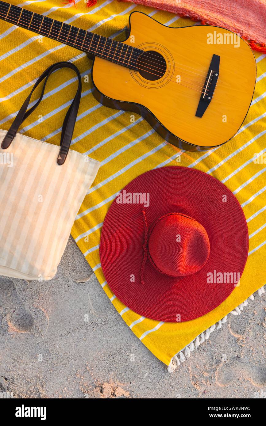 Un allestimento da spiaggia presenta una chitarra e un cappello rosso su una coperta gialla Foto Stock