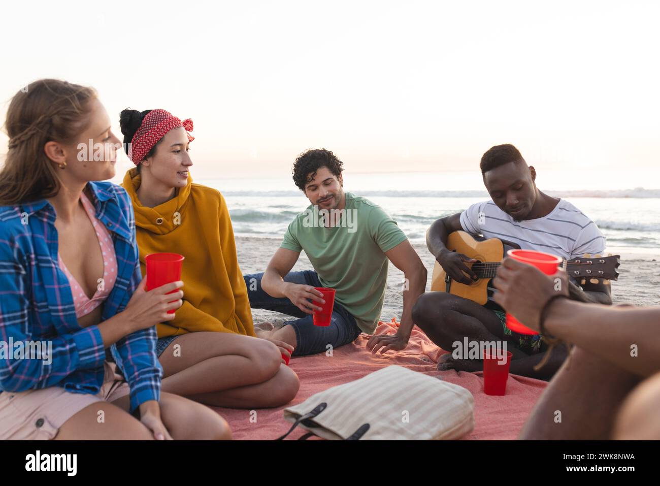 Amici diversi possono ascoltare musica sulla spiaggia al tramonto, fare una festa, con spazio per copiare Foto Stock